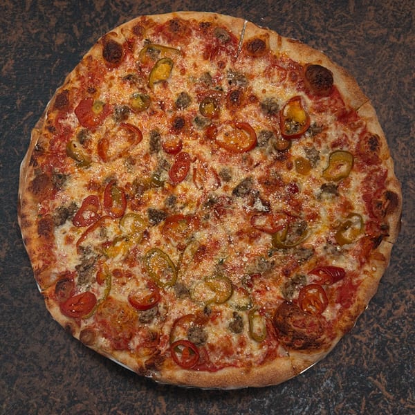 Whole pizza with sausage, cherry tomatoes, and sliced green peppers on a dark surface.