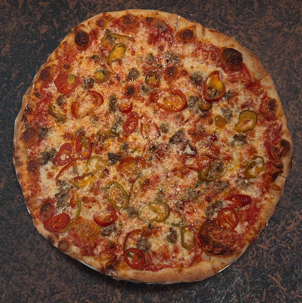 Whole pizza with sausage, cherry tomatoes, and sliced green peppers on a dark surface.